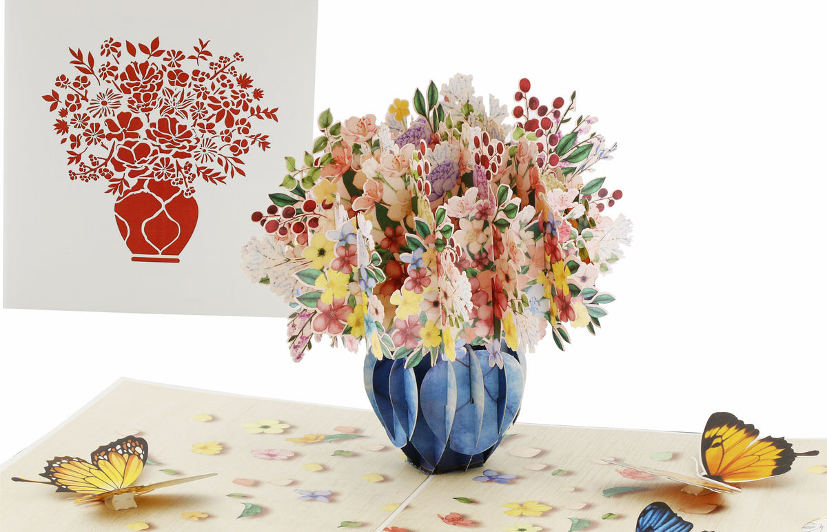 Aufgeklappte Pop-up-Karte mit einem bunten Blumenstrauß in blauer Vase und Schmetterlingen, daneben die weiße Kartenvorderseite mit Blumenstrauß-Scherenschnitt.