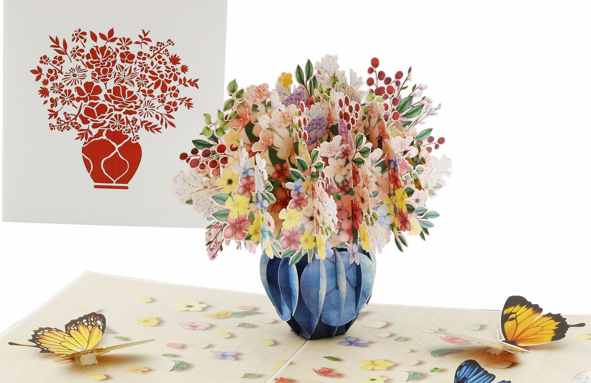 Aufgeklappte Pop-up-Karte mit einem bunten Blumenstrauß in blauer Vase und Schmetterlingen, daneben die weiße Kartenvorderseite mit Blumenstrauß-Scherenschnitt.