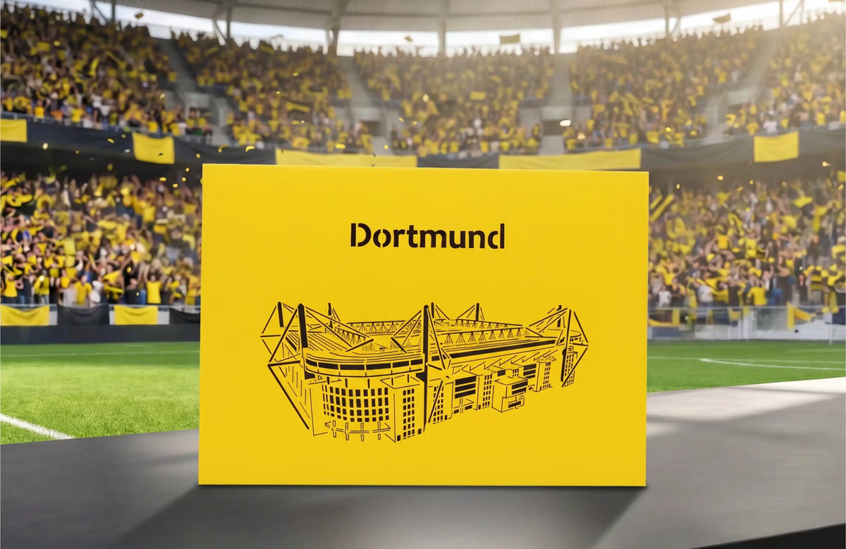 Gelbe Pop-up-Karte mit schwarzem Scherenschnitt eines Stadions und dem Schriftzug Dortmund auf einem Tisch im Fußballstadion.