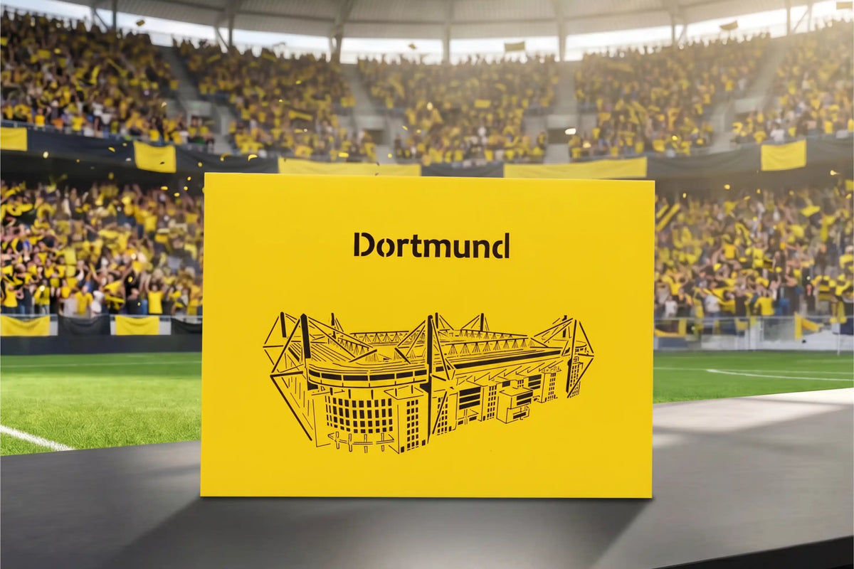Gelbe Pop-up-Karte mit schwarzem Scherenschnitt eines Stadions und dem Schriftzug Dortmund auf einem Tisch im Fußballstadion.