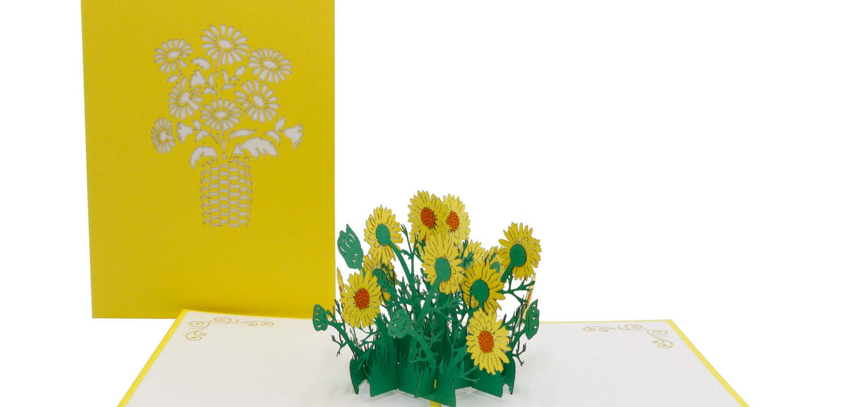 Aufgeklappte Pop-up-Karte mit gelben Gänseblümchen, daneben die gelbe Kartenvorderseite mit Blumen-Scherenschnitt.