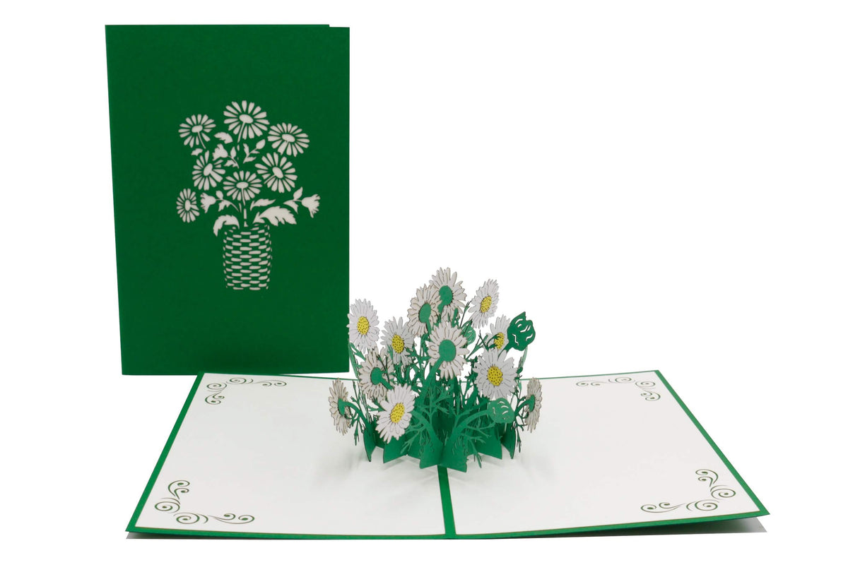 Aufgeklappte Pop-up-Karte mit weißen Gänseblümchen, daneben die grüne Kartenvorderseite mit Blumen-Scherenschnitt.