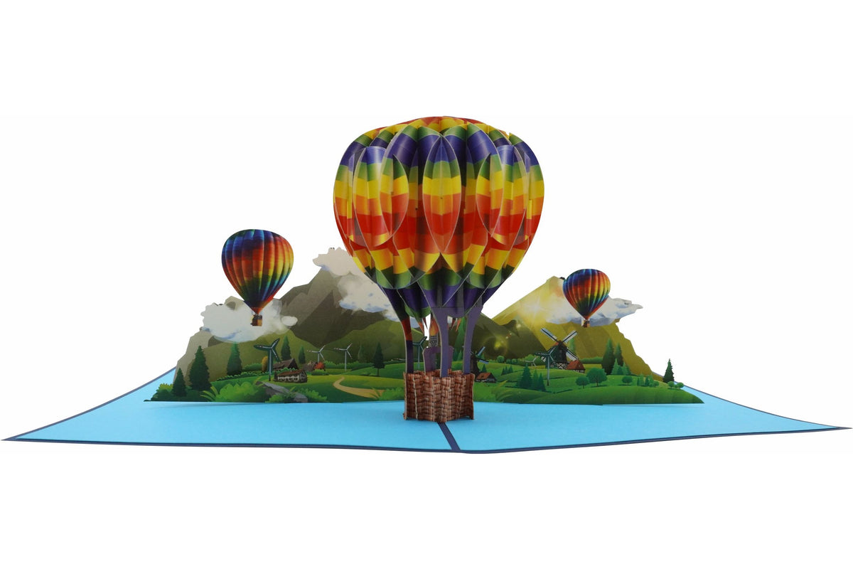 Aufgeklappte Pop-up-Karte mit einem bunten Heißluftballon über einer grünen Berglandschaft, seitlich fotografiert.