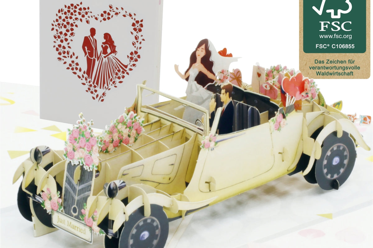Aufgeklappte Pop-up-Karte mit einem cremefarbenen Hochzeitsauto mit Blumenschmuck und Brautpaar, daneben die Kartenvorderseite mit Herz und FSC-Logo.