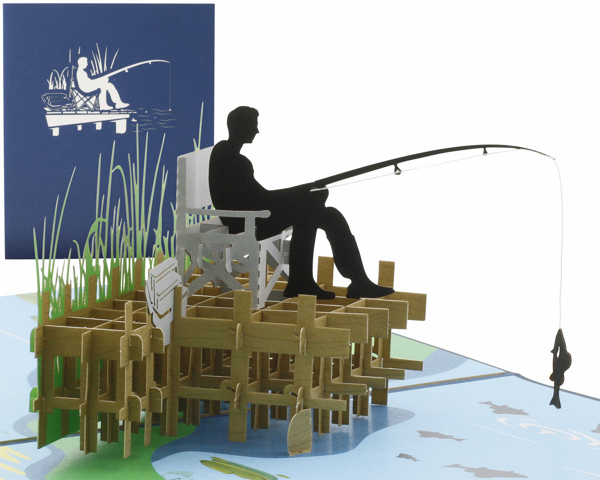 Pop-up-Karte mit einem Angler auf dem Steg, der auf einem Stuhl sitzt und angelt, im Hintergrund eine blaue Klappkarte mit einem Anglermotiv als Scherenschnitt.