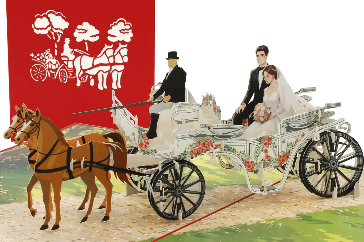 pop up karte mit brautpaar in der hochzeitskutsche. vorne mit einem kutscher und zwei pferden. Die Kutsche fährt aber einen alten Kopfsteinpflasterweg, umsäumt von einer Wiese mit Blumen.