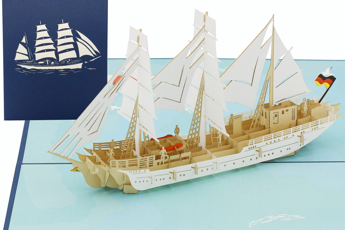 Aufgeklappte Pop-up-Karte mit dem Segelschiff Gorch Fock und Deutschlandflagge, dahinter die blaue Kartenvorderseite mit Segelschiff-Scherenschnitt.