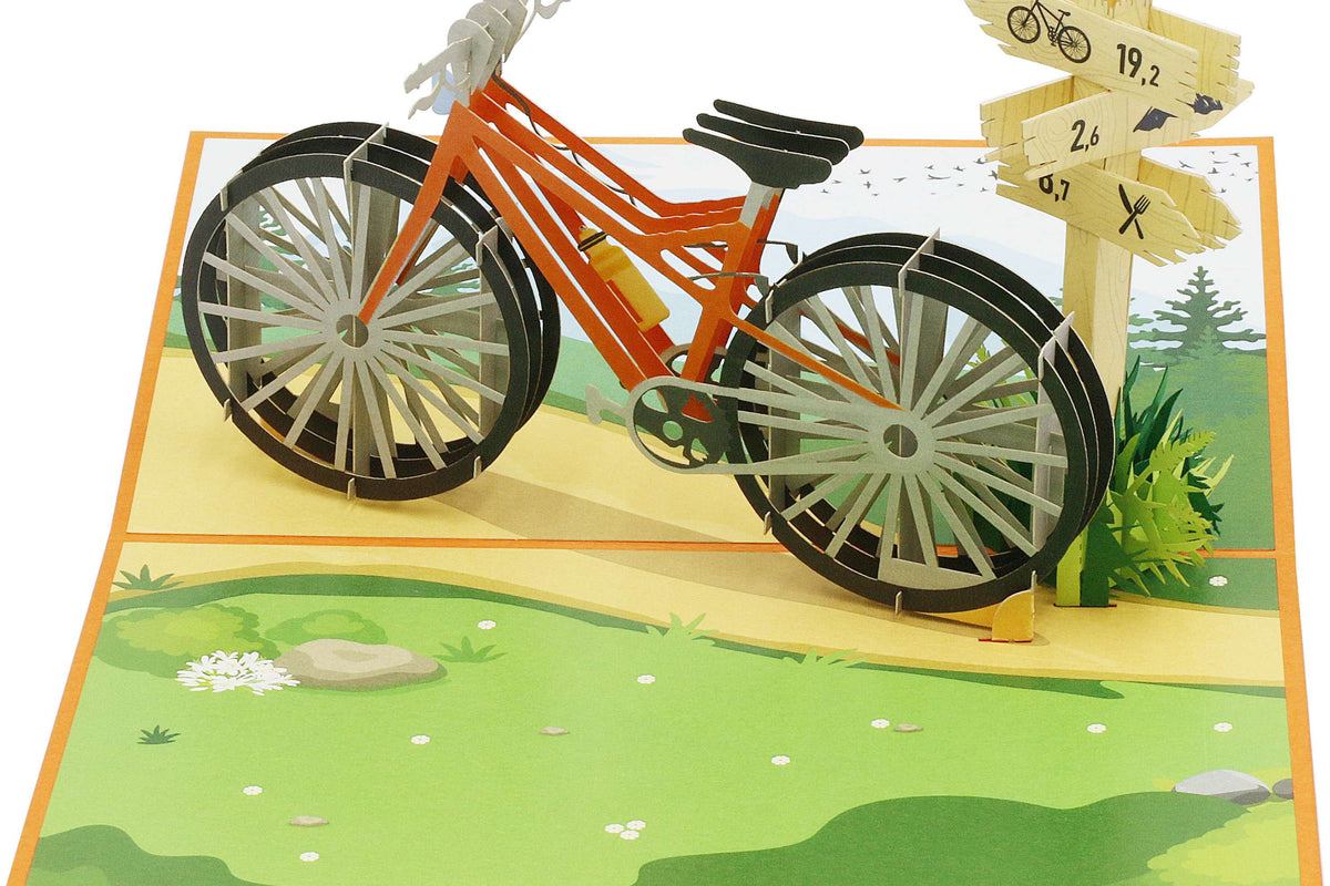 Aufgeklappte Pop-up-Karte mit orangem Fahrrad und Wegweiser aus Papier, schräg von oben fotografiert.