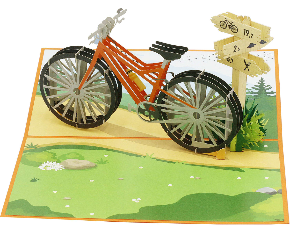 Aufgeklappte Pop-up-Karte mit orangem Fahrrad und Wegweiser aus Papier, schräg von oben fotografiert.