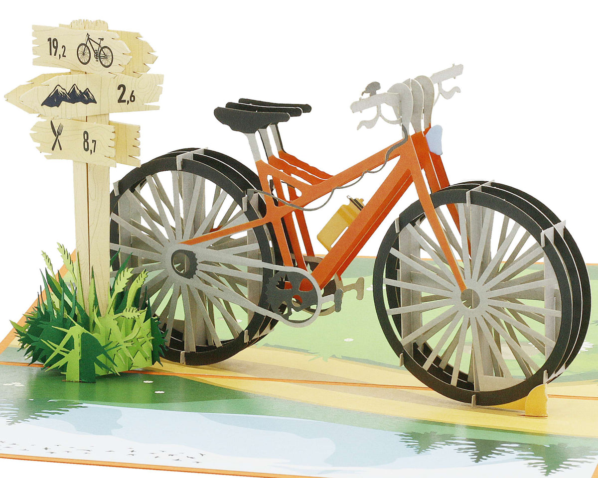 Aufgeklappte Pop-up-Karte mit einem orangen Fahrrad und einem Wegweiser mit Rad- und Wandersymbolen in einer Wiesenlandschaft.