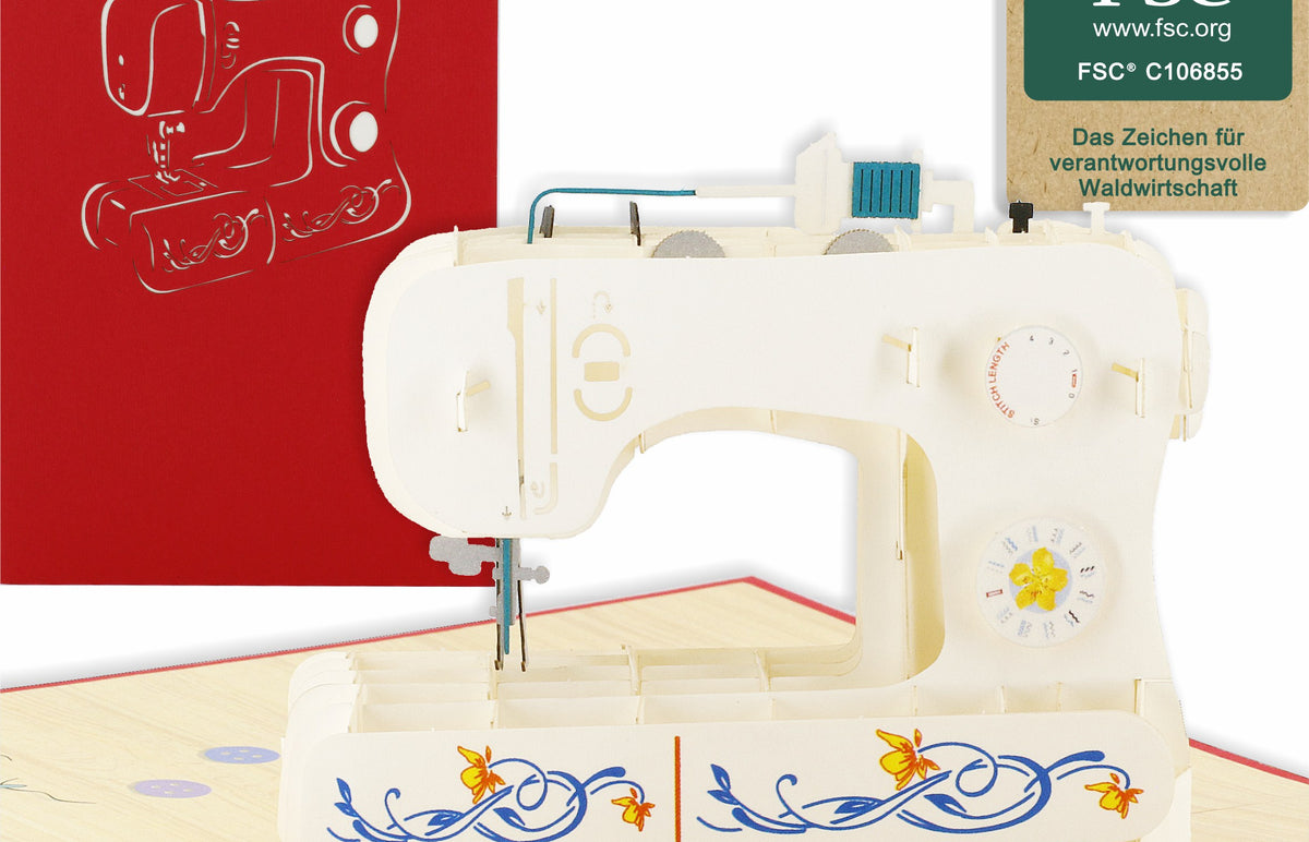 Aufgeklappte Pop-up-Karte mit einer weißen Nähmaschine mit Blumenmuster, daneben die rote Kartenvorderseite und das FSC-Logo.
