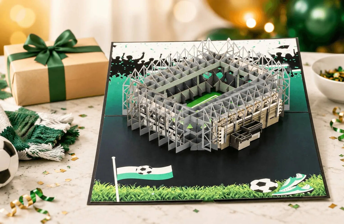 Aufgeklappte Pop-up-Karte zum Geburtstag mit detailreichem Stadionmodell, grün-weißem Rasenmuster und Fußballmotiven auf einem Tisch mit Geschenk und Dekoration