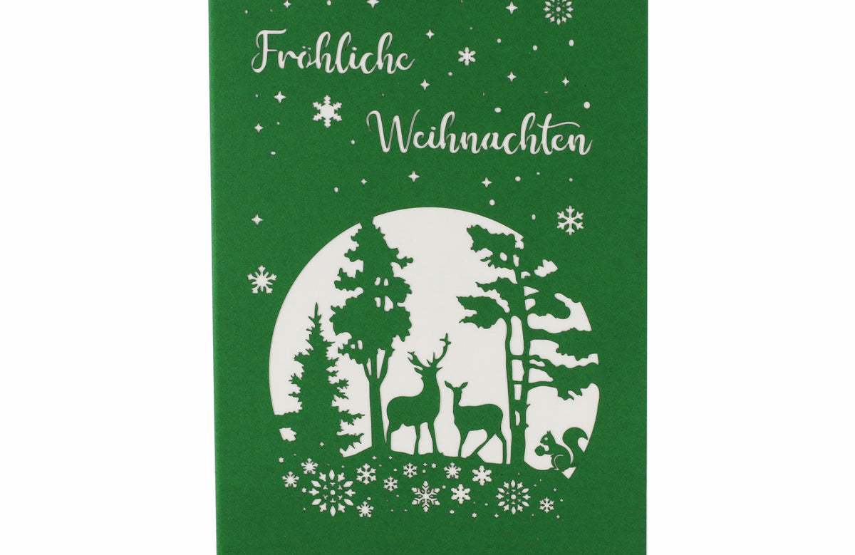 Grüne Vorderseite der Nikolaus Pop-up-Karte mit dem Schriftzug Fröhliche Weihnachten, Sternen, Schneeflocken und einem Winterwald mit Hirsch, Reh und Eichhörnchen als Scherenschnitt.