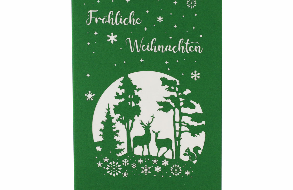 Vorderseite der Pop-up-Karte Winterwald mit Rentierschlitten: grüner Karton mit dem Gruß Fröhliche Weihnachten und einem verschneiten Wald mit Hirsch und Reh im filigranen Scherenschnitt.