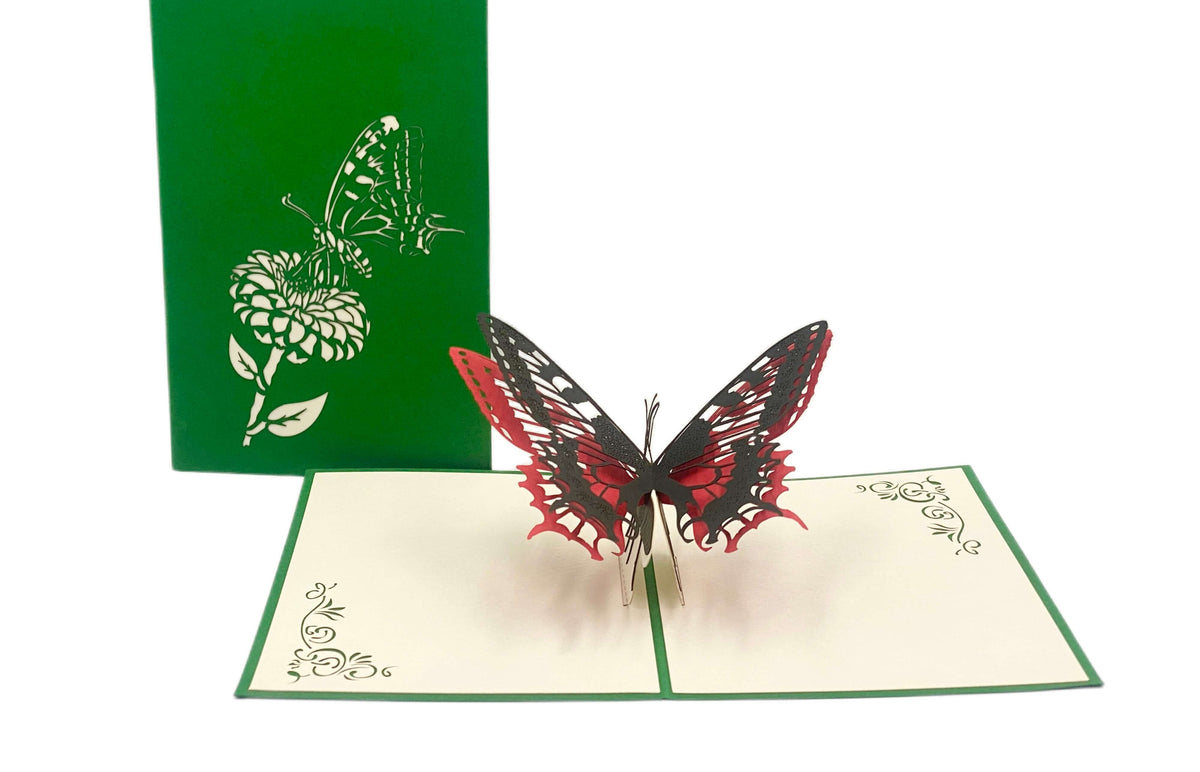 Aufgeklappte Pop-up-Karte mit rot-schwarzem Schmetterling, dahinter die grüne Kartenvorderseite mit Blüten-Scherenschnitt.