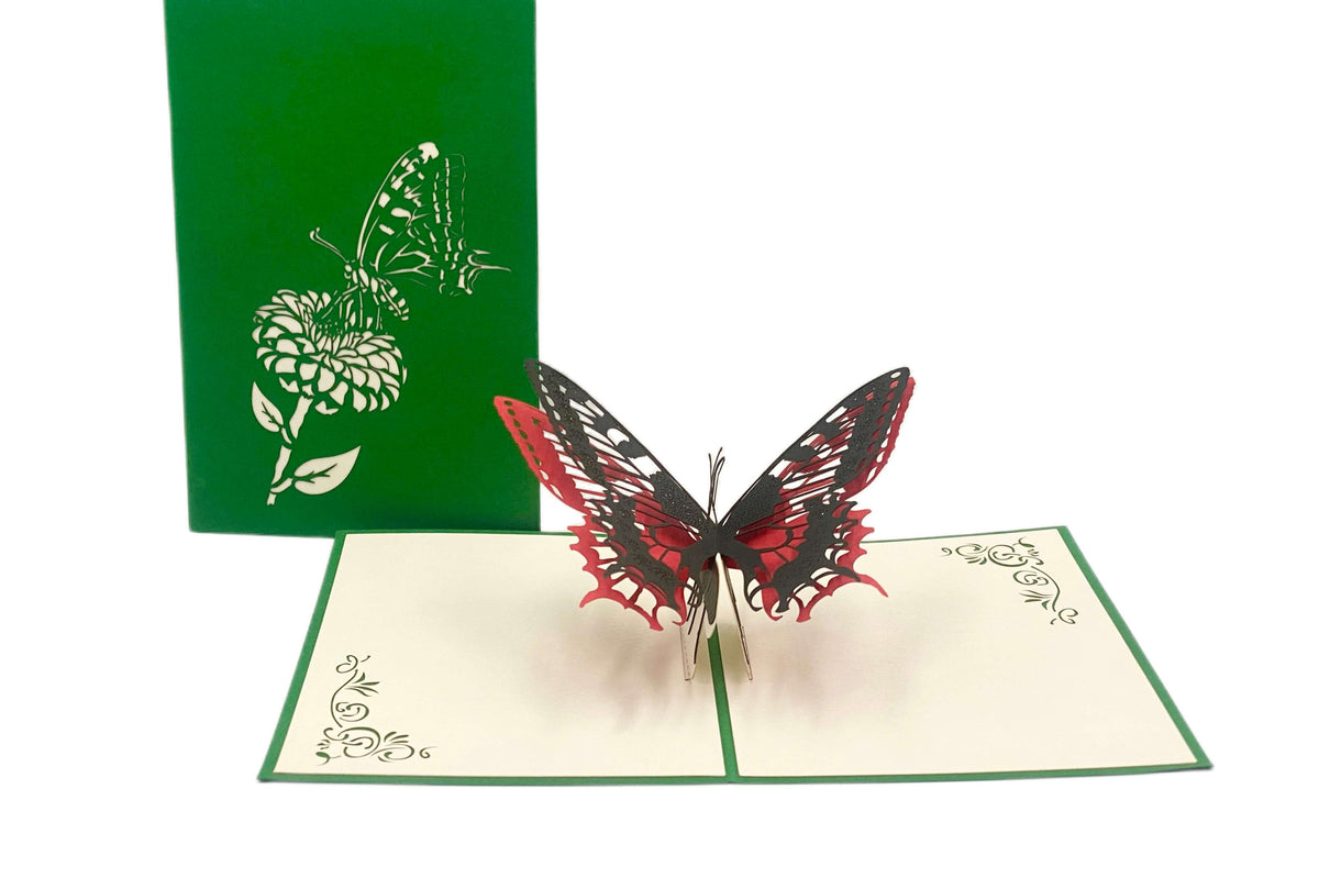 Aufgeklappte Pop-up-Karte mit rot-schwarzem Schmetterling, dahinter die grüne Kartenvorderseite mit Blüten-Scherenschnitt.