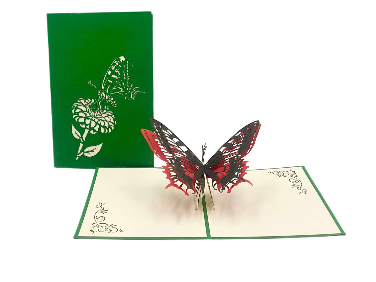 Aufgeklappte Pop-up-Karte mit rot-schwarzem Schmetterling, dahinter die grüne Kartenvorderseite mit Blüten-Scherenschnitt.