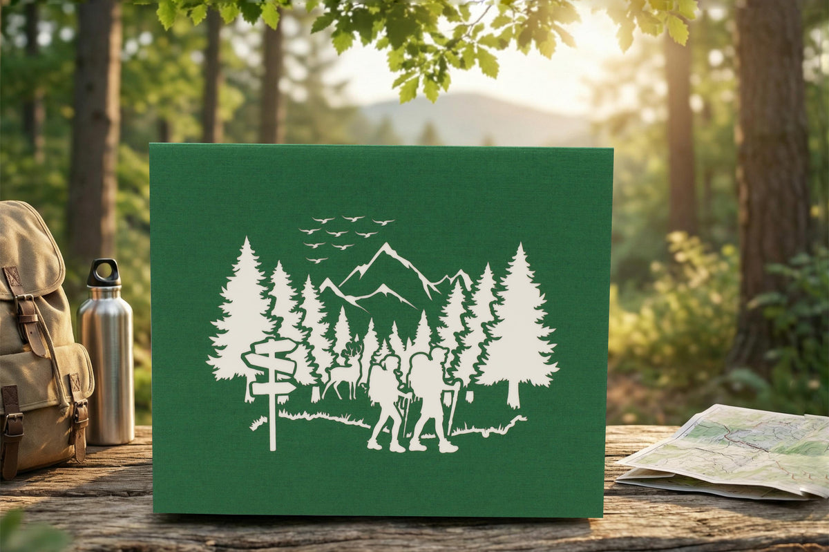 Grüne Klappkarte mit einem Wald, Bergen und 2 Wandersleuten in der Natur als Scherenschnitt. Die Pop Up Karte steht auf einer Bank in der Natur und im Hintergrund ist ein Wald.