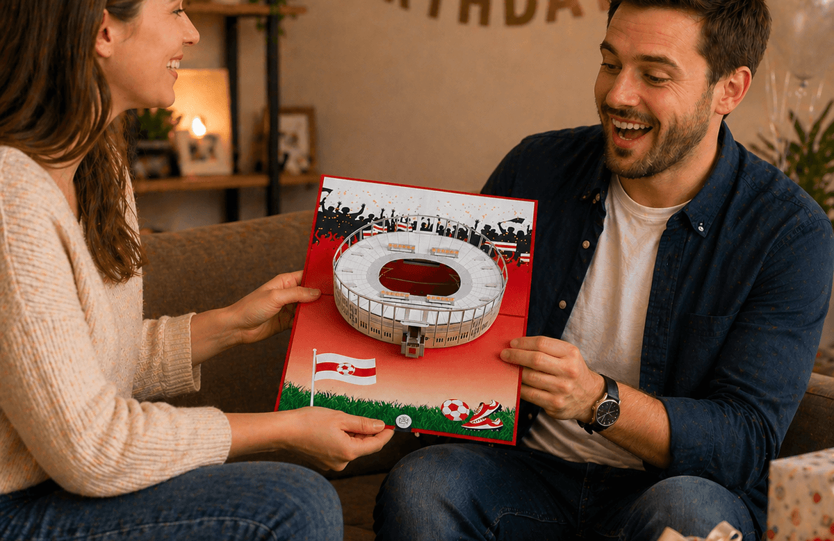 Im Wohnzimmer schenkt die Frau einem Mann eine Pop UP Geburtstagskarte mit einem Stuttgarter Fußballstadion
