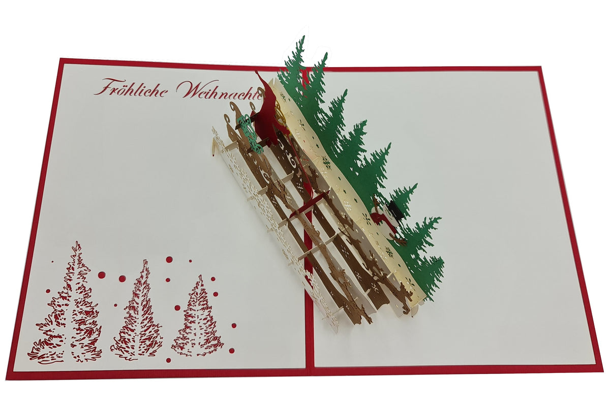 Aufgeklappte Pop-up-Karte mit Weihnachtsmann im Rentierschlitten, grünen Tannen und dem Schriftzug Fröhliche Weihnachten auf weißem Papier mit rotem Rand.