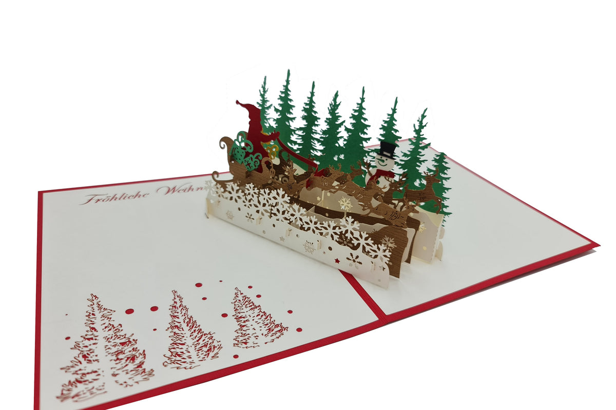 Aufgeklappte Pop-up-Karte mit fliegendem Rentierschlitten und Tannenwald aus Papier, schräg von der Seite fotografiert.