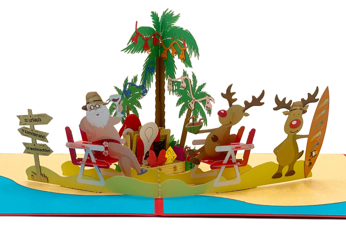 Nahaufnahme der aufgeklappten Pop-up-Karte: Weihnachtsmann im Liegestuhl mit Sonnenhut unter einer mit Christbaumkugeln geschmückten Palme, daneben zwei Rentiere mit Surfbrett am Sandstrand.