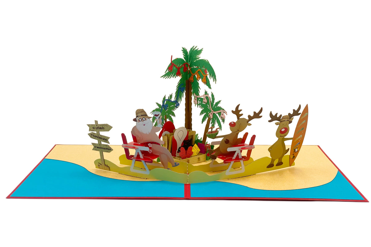 Aufgeklappte Pop-up-Karte mit Weihnachtsmann und Rentieren am Strand, Palmen mit Christbaumkugeln, gelbem Sand und türkisem Meer.