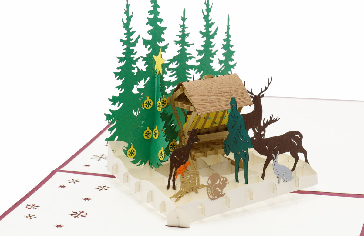 Aufgeklappte Pop-up-Karte mit Futterkrippe, Hirsch und Rehen im verschneiten Wald, seitlich fotografiert.
