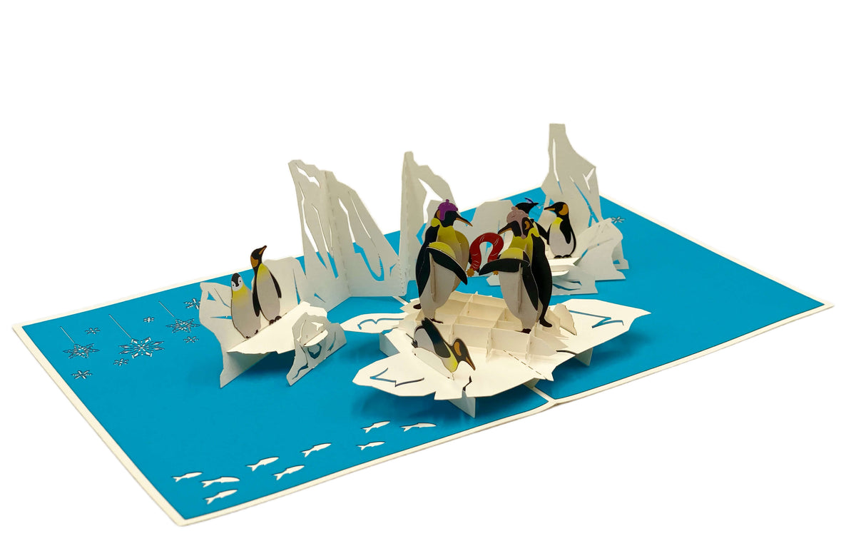 Aufgeklappte Pop-up-Karte mit blauem Innenteil: eine Gruppe Pinguine auf weißen Eisschollen.