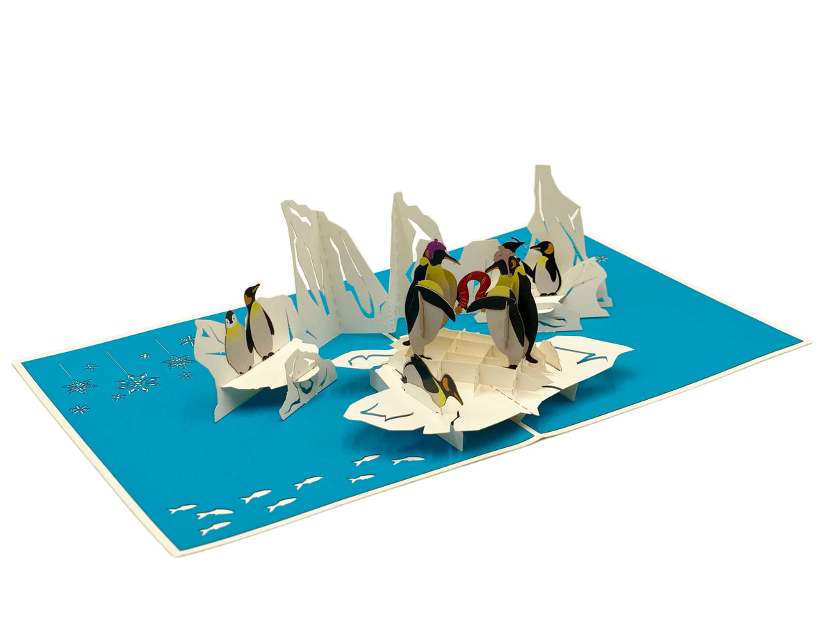 Aufgeklappte Pop-up-Karte mit blauem Innenteil: eine Gruppe Pinguine auf weißen Eisschollen.