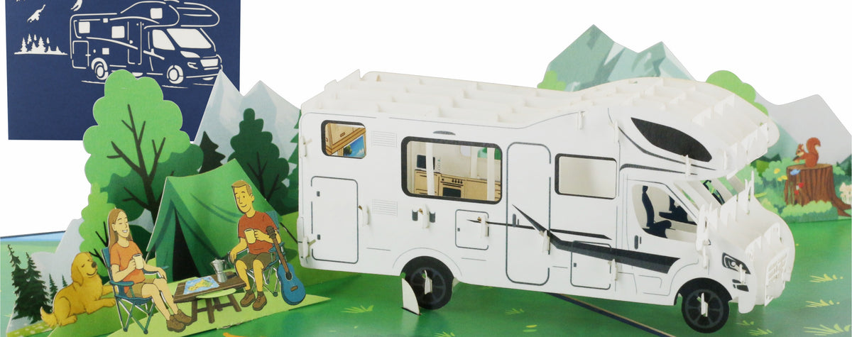 Aufgeklappte Pop-up-Karte mit weißem Wohnmobil in einer Berglandschaft, davor Camper am Lagerfeuer, dahinter die blaue Kartenvorderseite mit Wohnmobil-Scherenschnitt.