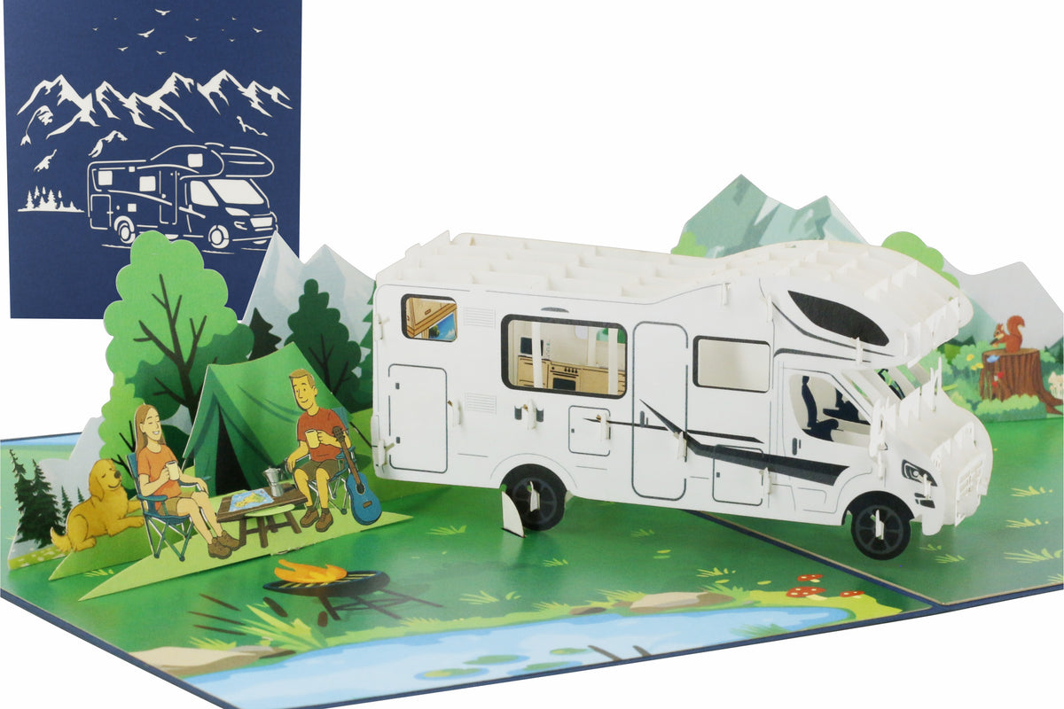 Aufgeklappte Pop-up-Karte mit weißem Wohnmobil in einer Berglandschaft, davor Camper am Lagerfeuer, dahinter die blaue Kartenvorderseite mit Wohnmobil-Scherenschnitt.