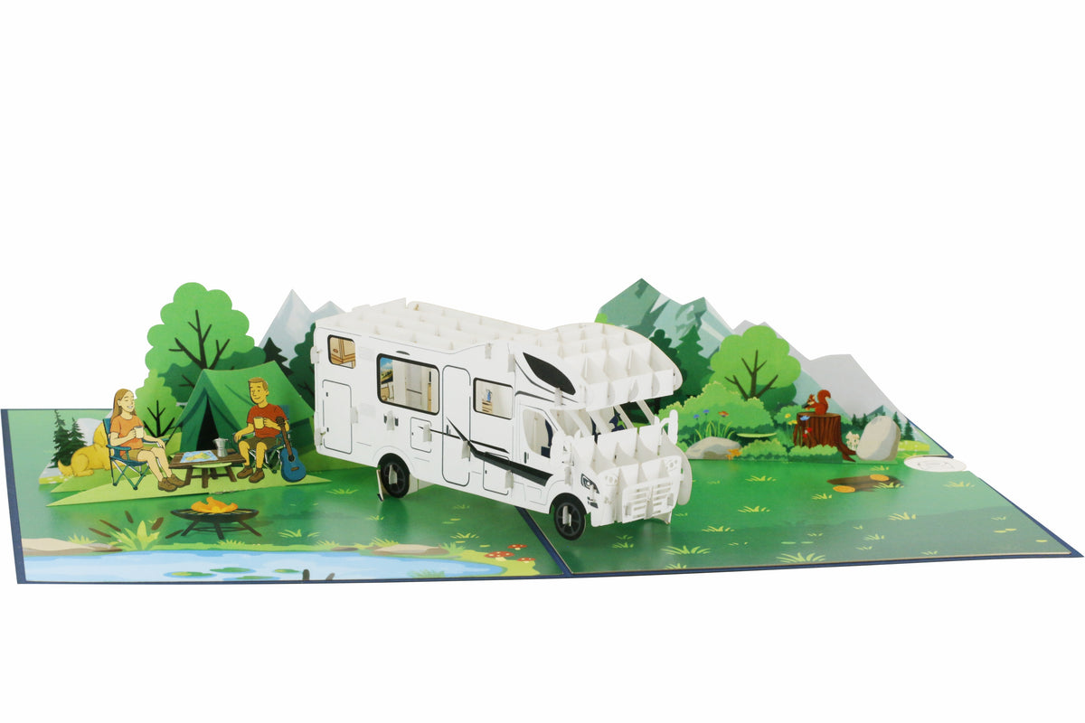 Aufgeklappte Pop-up-Karte mit weißem Wohnmobil, Bäumen und Bergen aus Papier, frontal fotografiert.