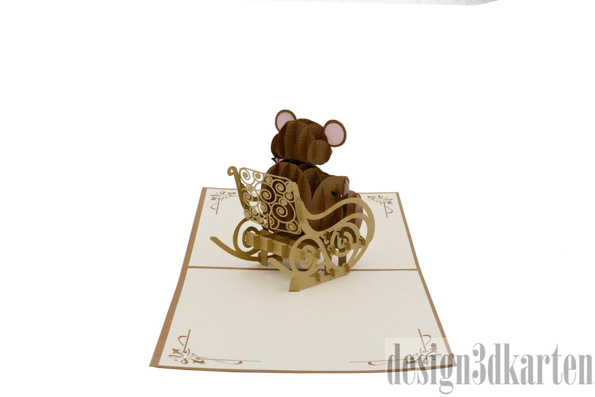 Aufgeklappte Pop-up-Karte mit Teddybär im Schaukelstuhl, schräg von der Seite fotografiert.