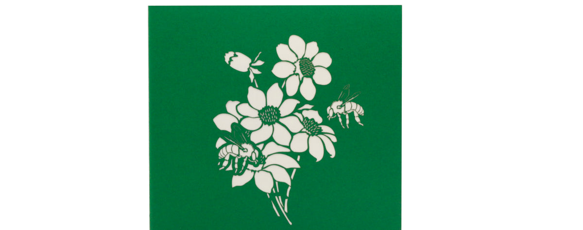 Grüne Kartenvorderseite mit Blüten und einer Biene als Scherenschnitt.