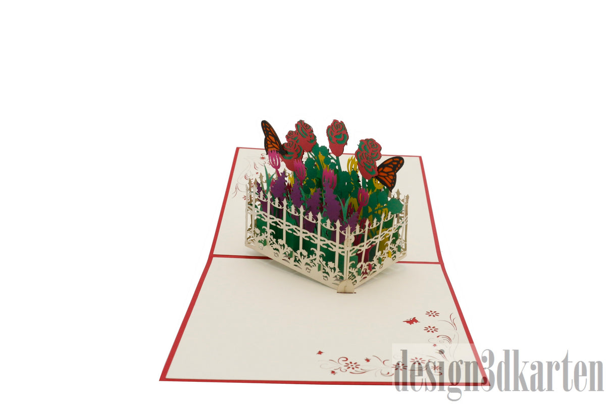 Aufgeklappte Pop-up-Karte mit rotem Rand: bunter Blumengarten hinter einem weißen Gartenzaun mit Schmetterlingen.