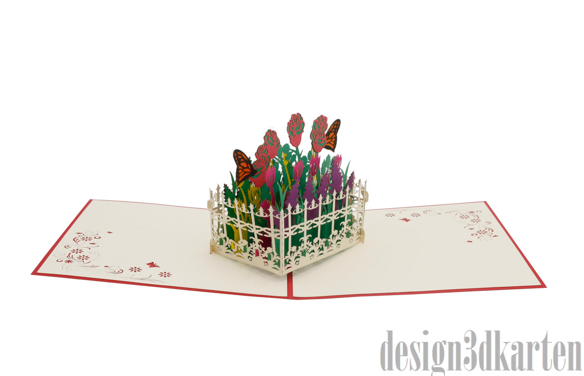 Aufgeklappte Pop-up-Karte mit Blumengarten, Gartenzaun und Schmetterlingen aus Papier, schräg fotografiert.