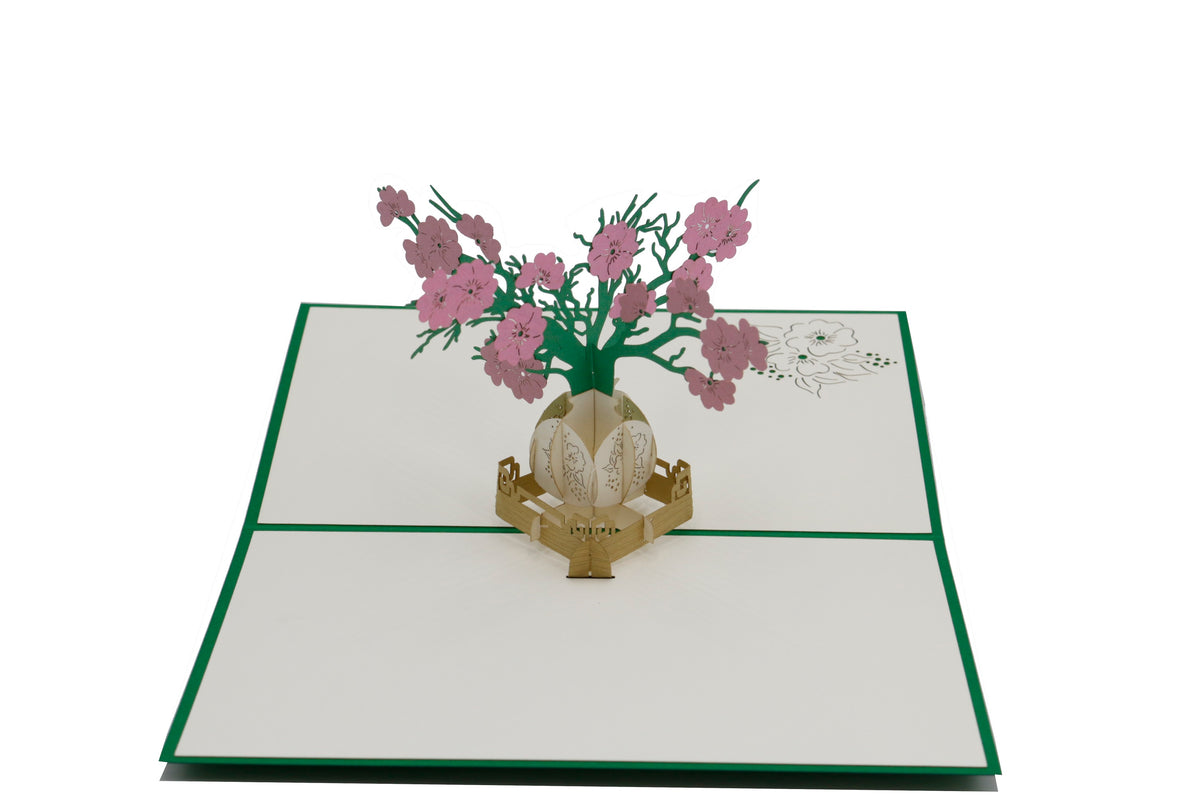 Aufgeklappte Pop-up-Karte mit rosa und weißen Blüten in einer goldenen Vase, von schräg oben fotografiert.
