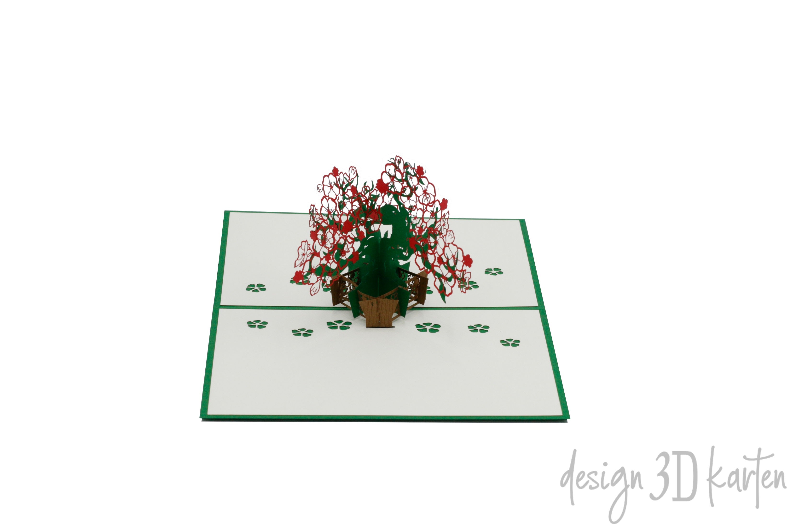 Aufgeklappte weiße Pop-up-Karte mit grünem Rand und einem blühenden Bonsai-Baum mit roten und weißen Blüten in einem Topf, auf der Kartenfläche verstreute Blütenblätter.