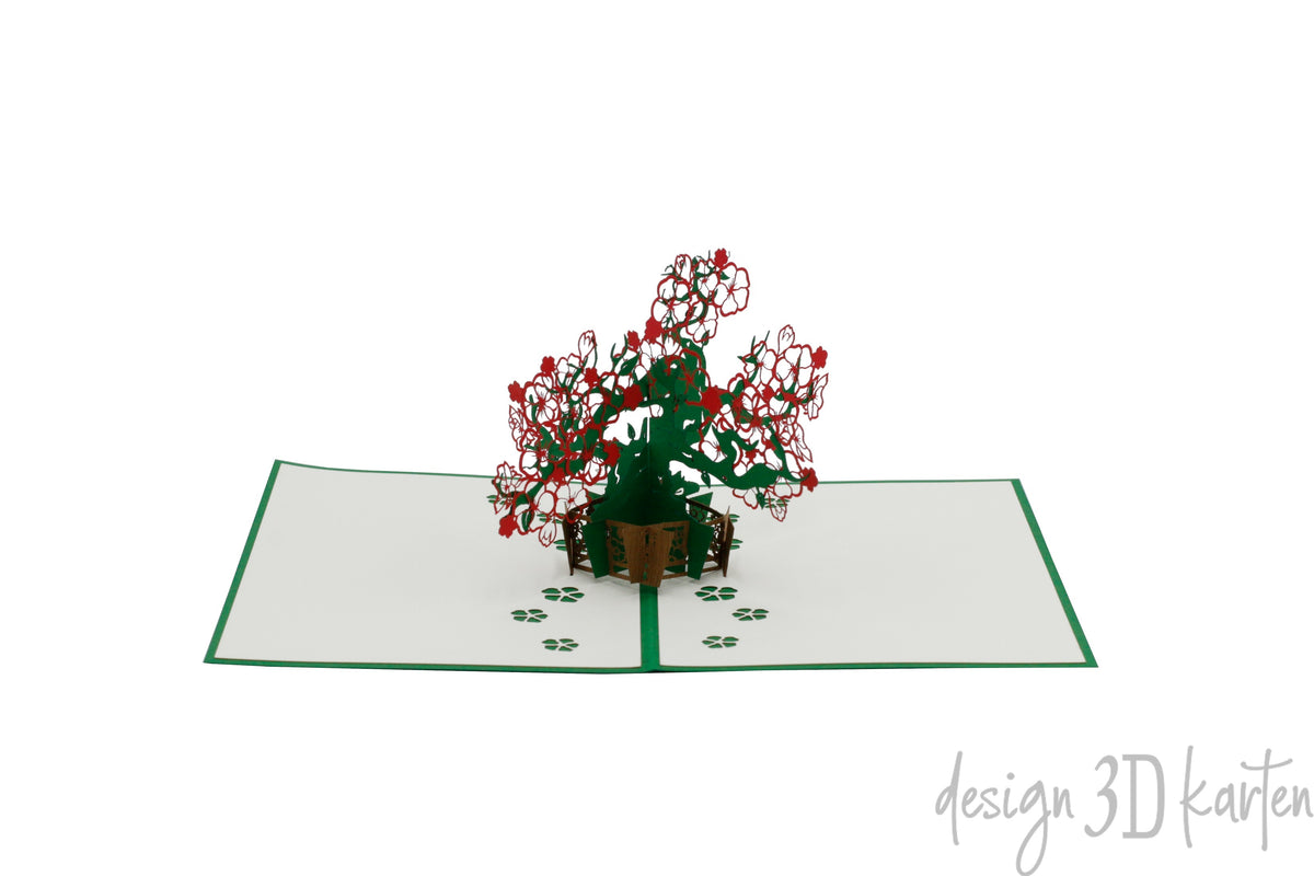 Aufgeklappte Pop-up-Karte mit filigranem Blumenbonsai aus Papier, schräg von der Seite fotografiert.