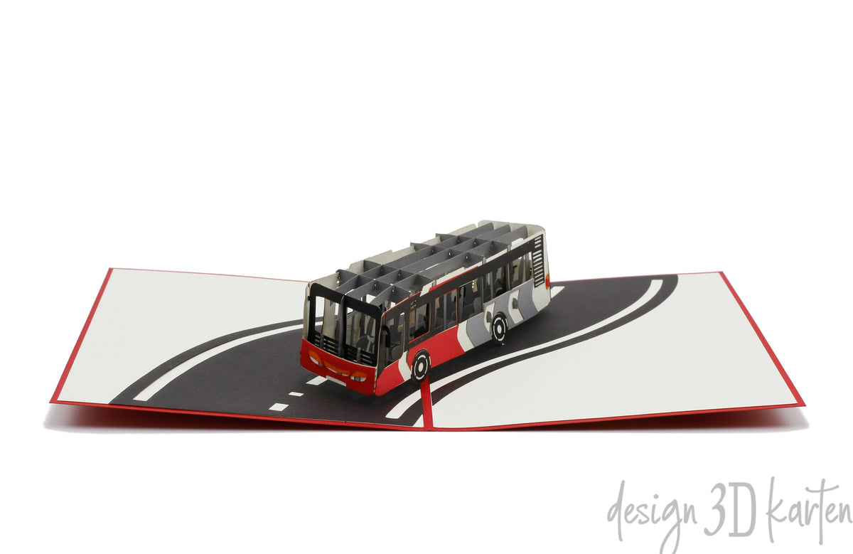Aufgeklappte Pop-up-Karte mit einem Linienbus auf einer geschwungenen Straße, schräg von oben fotografiert.