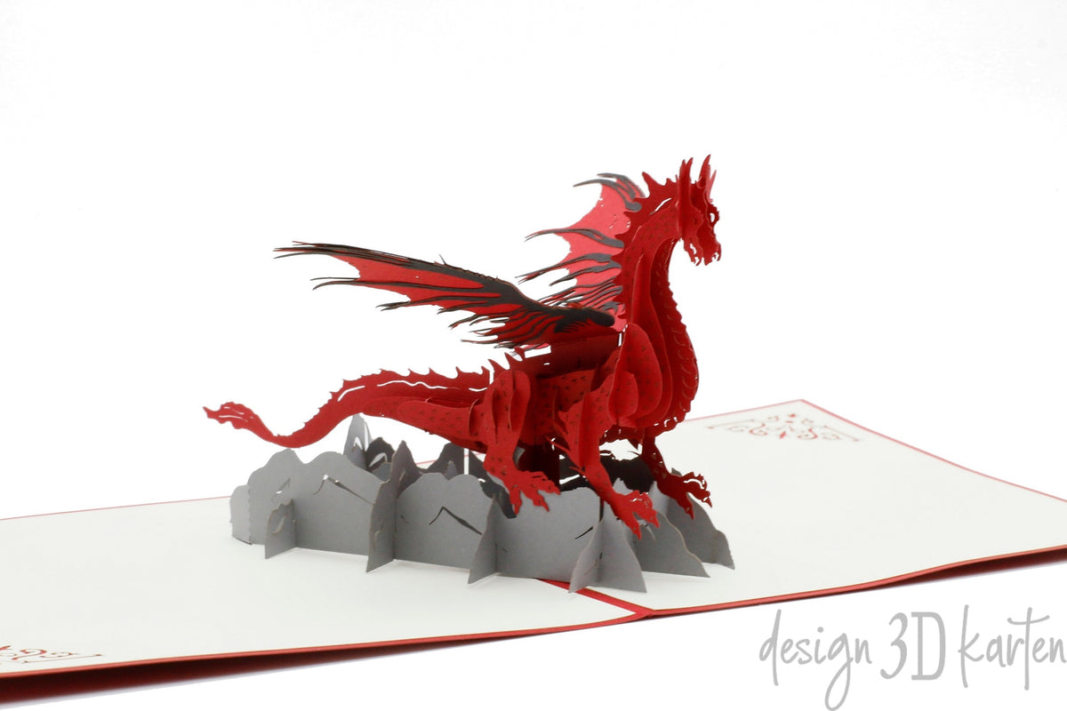 Aufgeklappte Pop-up-Karte mit einem roten Drachen auf grauen Felsen, seitlich fotografiert.