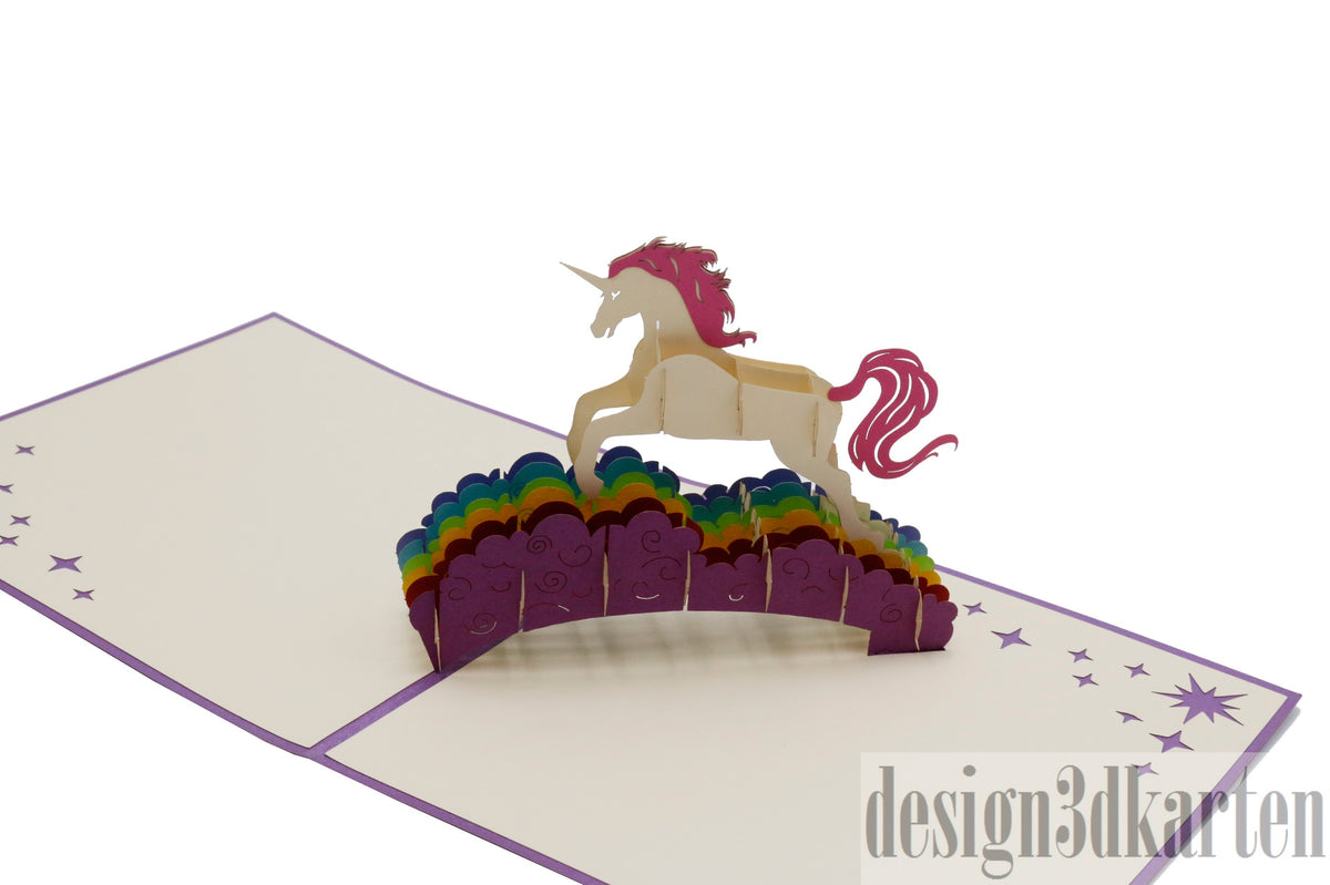 Aufgeklappte Pop-up-Karte mit lila Rand: ein weißes Einhorn mit pinker Mähne auf einer Regenbogenbrücke.