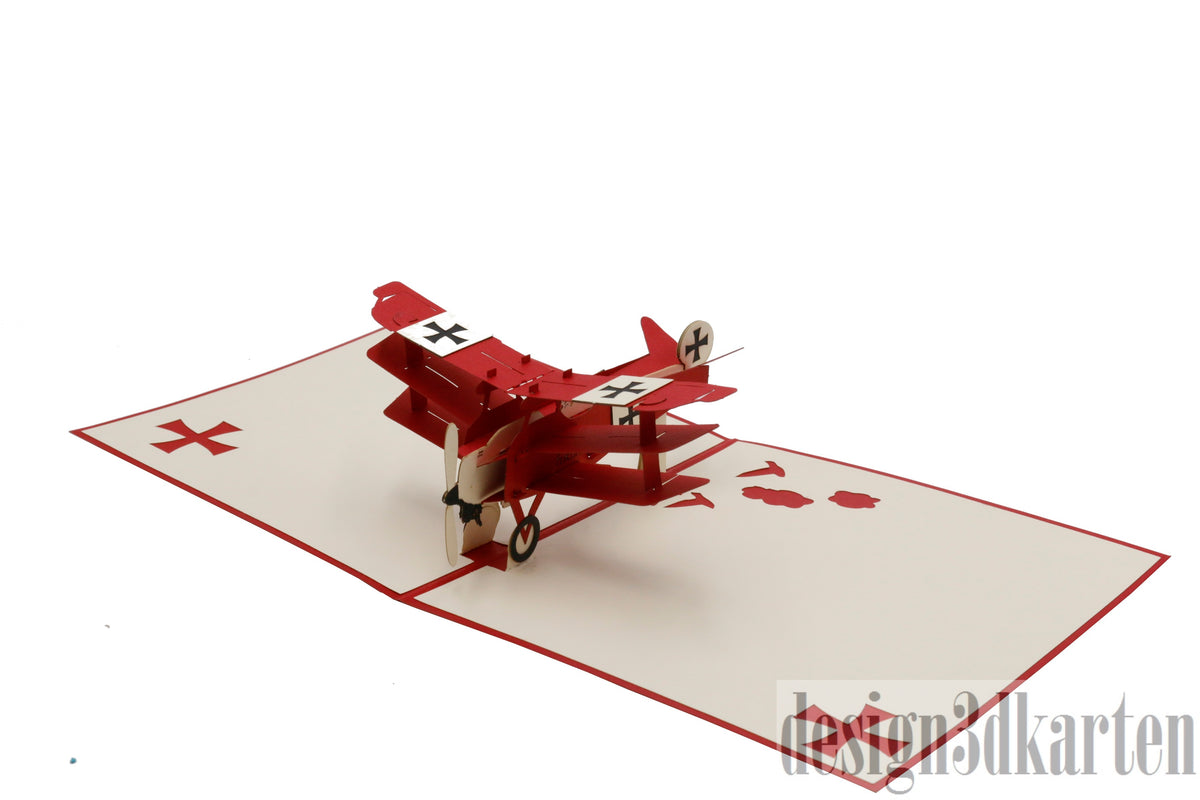 Aufgeklappte Pop-up-Karte mit einem roten Dreidecker-Flugzeug aus Papier, seitlich fotografiert.