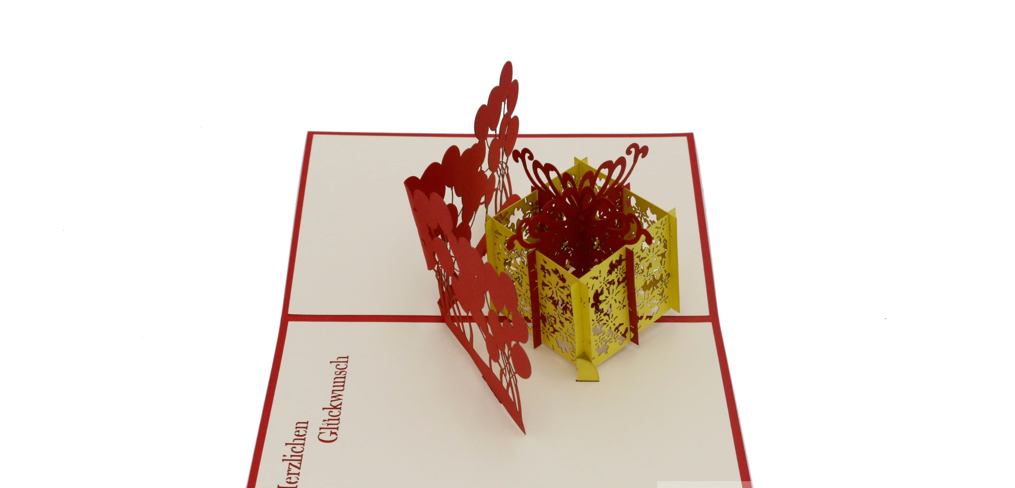 Aufgeklappte Pop-up-Karte mit gelber Geschenkbox und Luftballons, seitlich fotografiert.