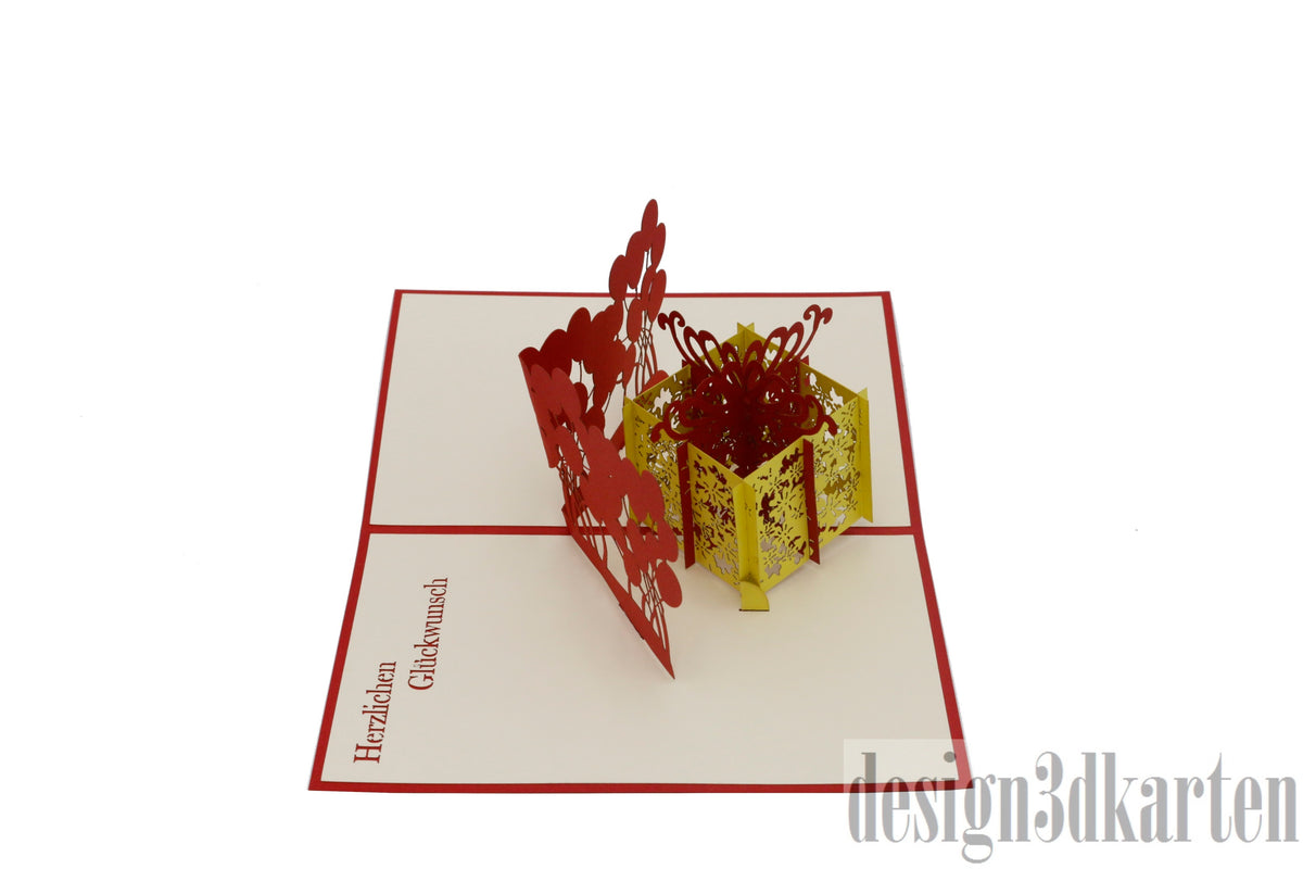 Aufgeklappte Pop-up-Karte mit gelber Geschenkbox und Luftballons, seitlich fotografiert.