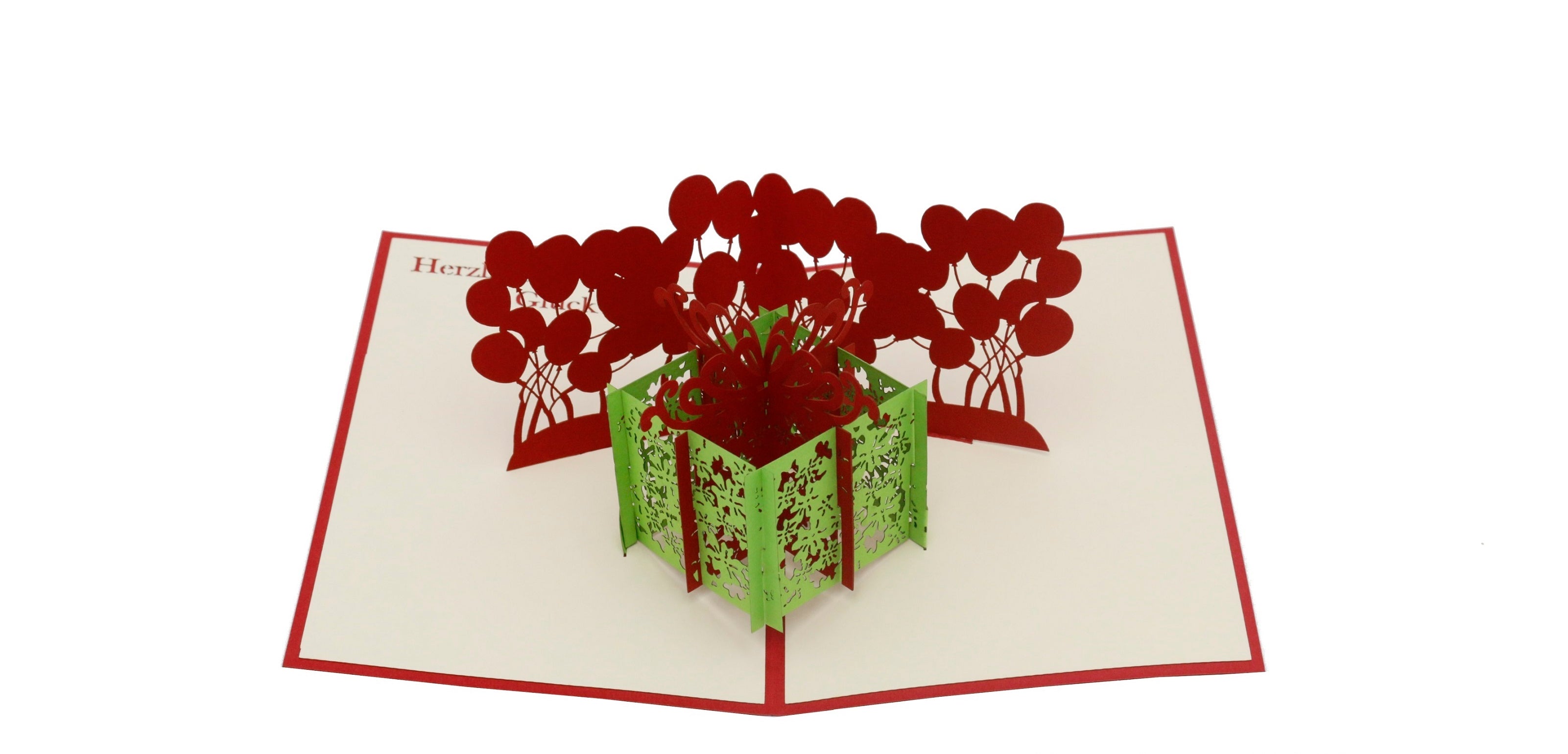 Aufgeklappte Pop-up-Karte mit grüner Geschenkbox und roten Luftballons, frontal fotografiert.