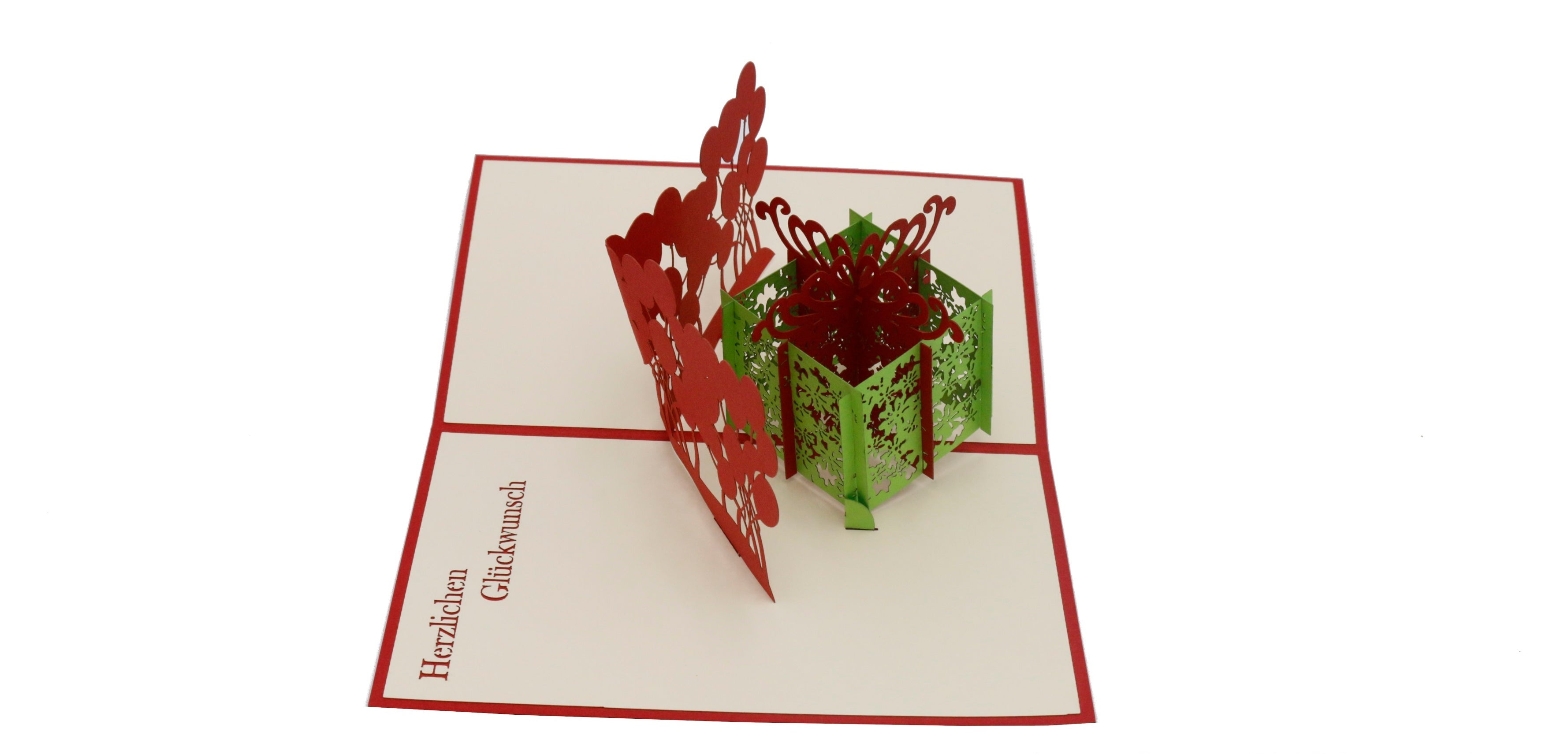 Aufgeklappte Pop-up-Karte mit grüner Geschenkbox und roten Luftballons, schräg von der Seite fotografiert.