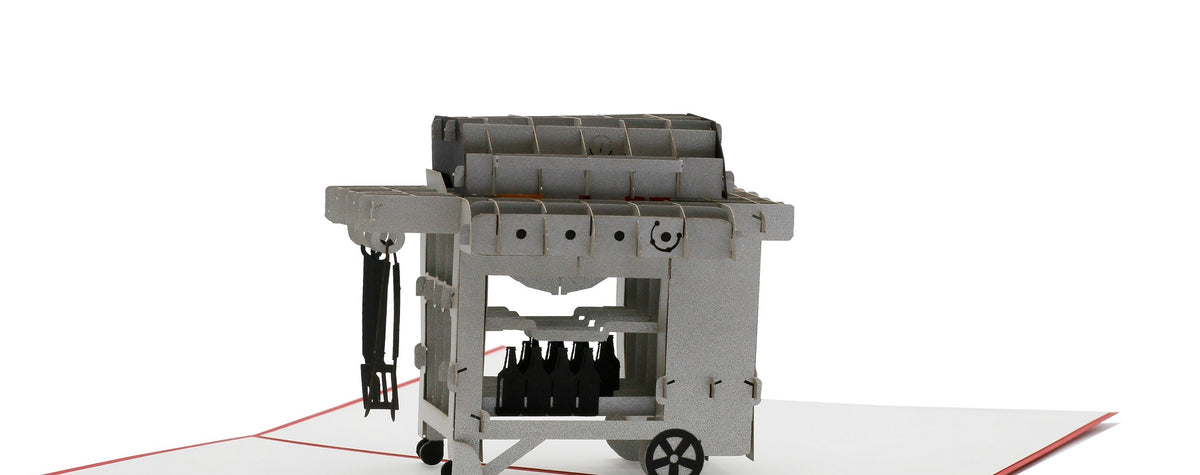 Aufgeklappte Pop-up-Karte mit einem Gasgrill aus Papier, seitlich fotografiert.