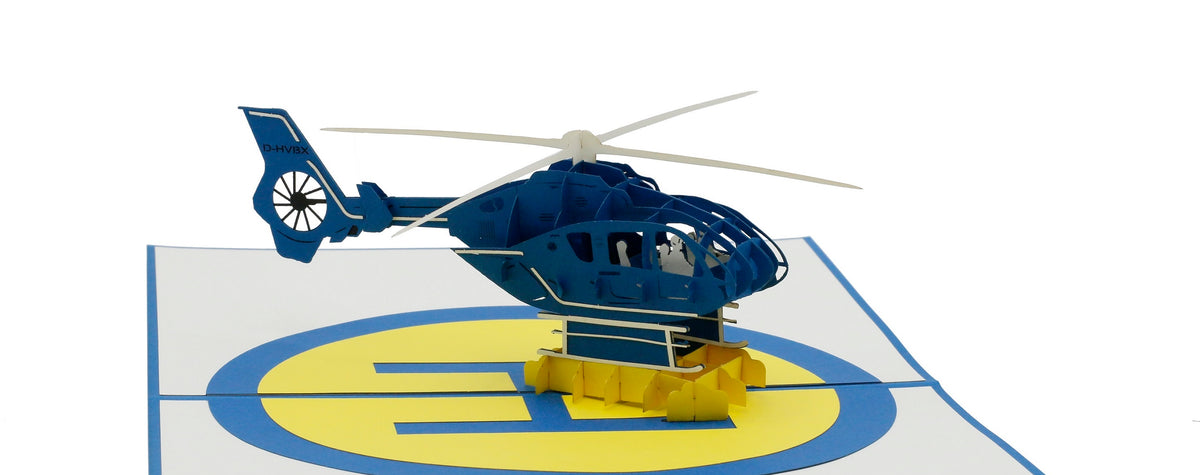 Aufgeklappte Pop-up-Karte mit einem blauen Hubschrauber auf einem gelb-blauen Landeplatz.